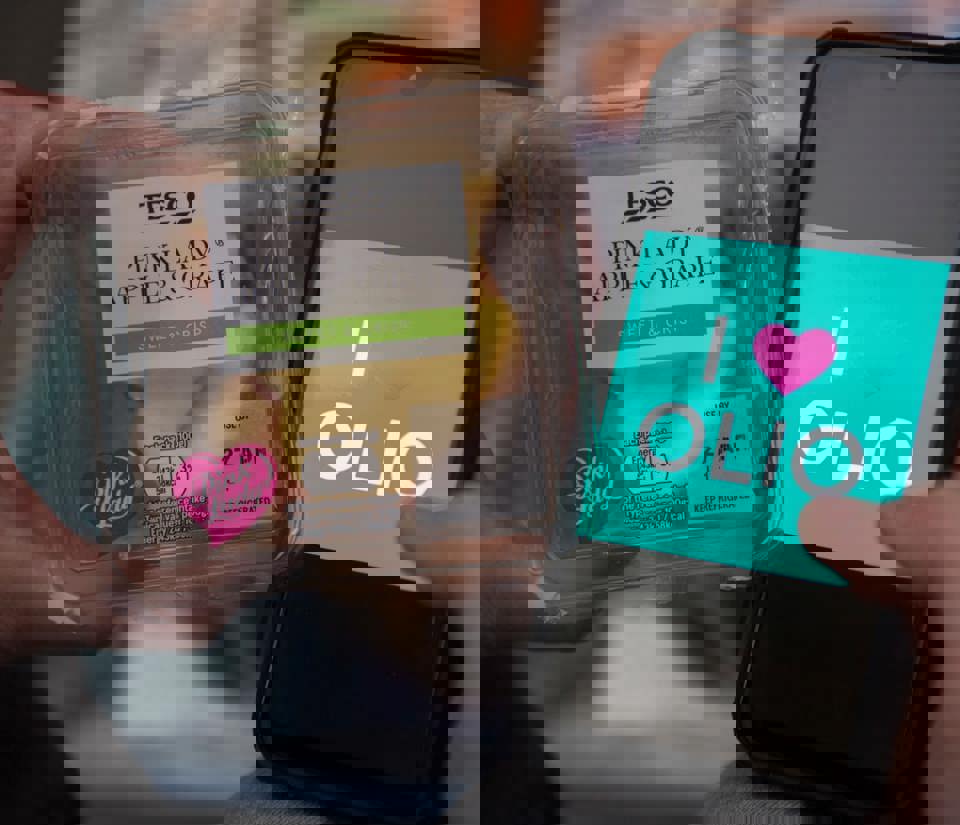 Person holding an iPhone displaying I love Olio alongside a pack of Tesco pink lady apple and grape