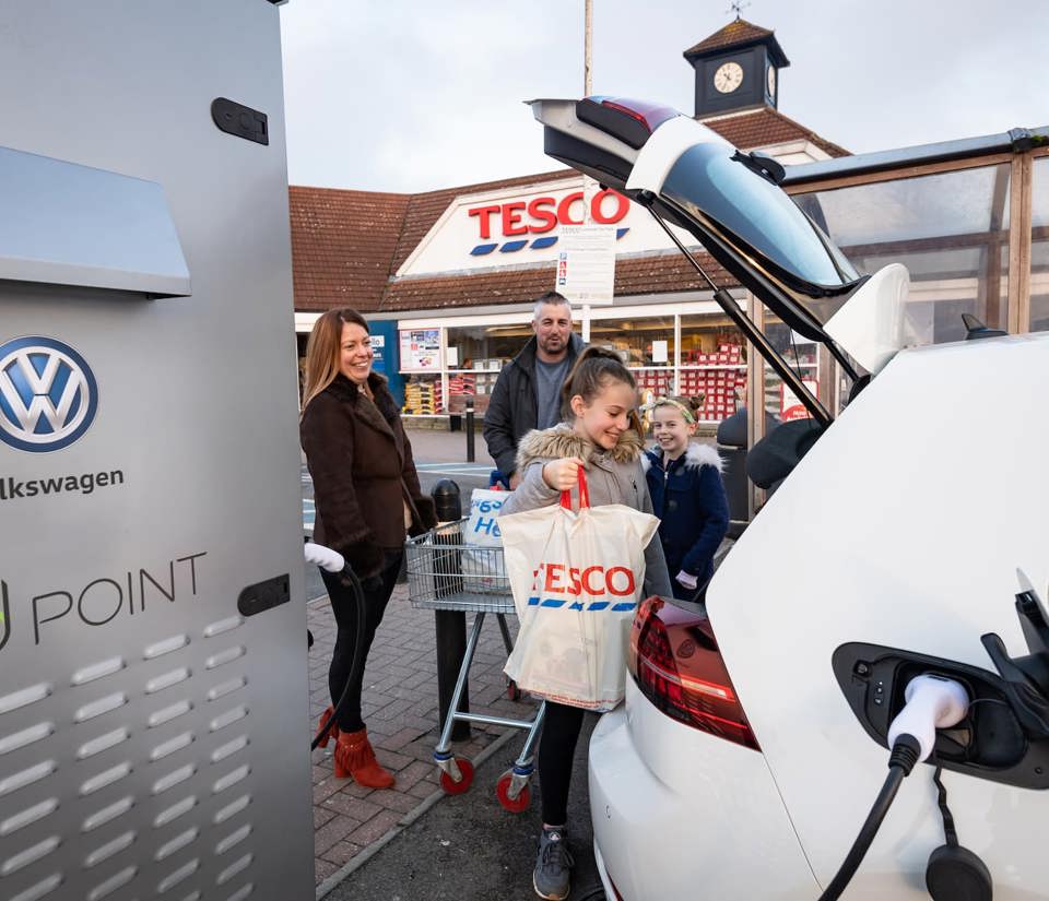 Family loading their Tesco shopping into the boot of their charging electric car