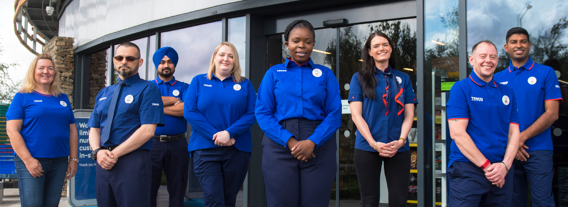 A group of Tesco colleagues standing smiling outside the store door